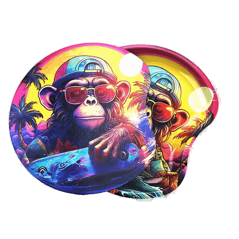 The image displays a strikingly colorful rolling tray featuring a bold, vibrant design with a monkey wearing sunglasses and palm trees in the background. The tray is circular and includes a lid, making it a functional accessory for rolling papers.